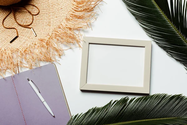 Vue du dessus des feuilles de palmier vert, cadre carré, cahier violet et chapeau de soleil sur fond blanc — Photo de stock