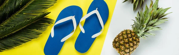 Top view of green palm leaves, pineapples, blue flip flops on white and yellow background, panoramic shot — Stock Photo