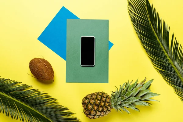 Вид сверху на зеленые пальмовые листья, смартфон, кокос, ананас на красочном фоне — стоковое фото