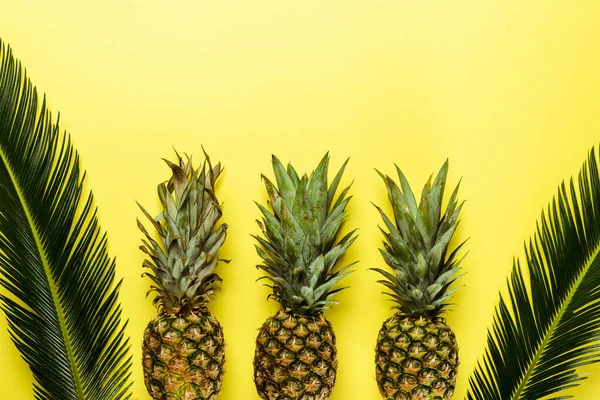 Top view of green palm leaves and ripe pineapples on yellow background — Stock Photo
