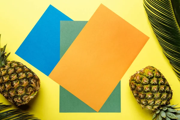 Vue de dessus des feuilles de palmier vert et des ananas mûrs sur fond coloré — Photo de stock