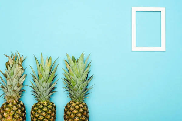 Top view of ripe pineapples near square empty frame on blue background — Stock Photo