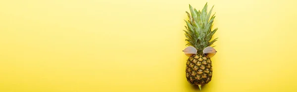 Top view of ripe pineapple in sunglasses on yellow background, panoramic shot — Stock Photo