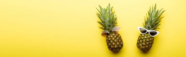 Vista dall'alto di ananas maturi in occhiali da sole su sfondo giallo, colpo panoramico — Foto stock