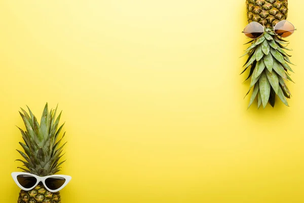 Top view of ripe pineapples in sunglasses on yellow background — Stock Photo