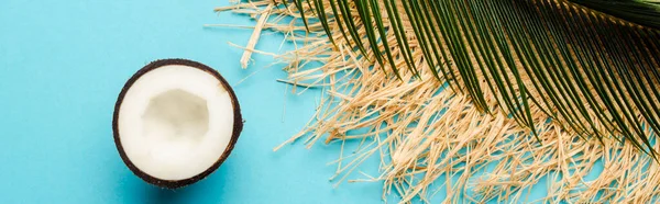 Top view of green palm leaf, coconut half, straw hat on blue background, panoramic shot — Stock Photo