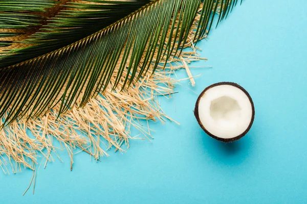 Vista dall'alto di foglia di palma verde, mezza noce di cocco, cappello di paglia su sfondo blu — Foto stock