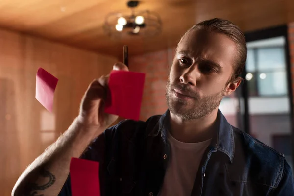 Selective focus of tattooed businessman looking at sticky note — Stock Photo