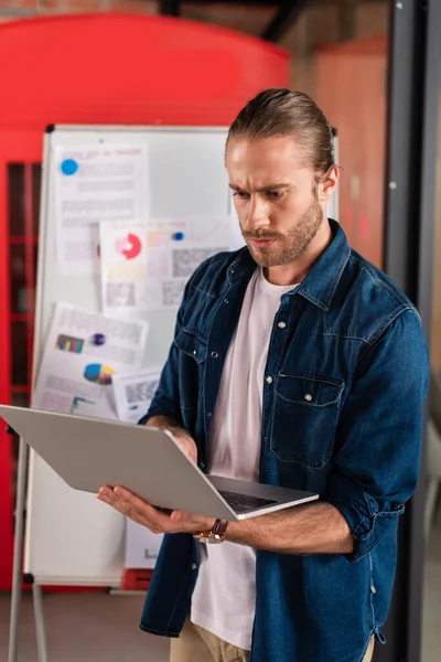 Handsome businessman using laptop near charts and graphs — Stock Photo