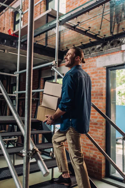 Selective focus of smiling businessman holding boxes while walking on stairs in office — Stock Photo