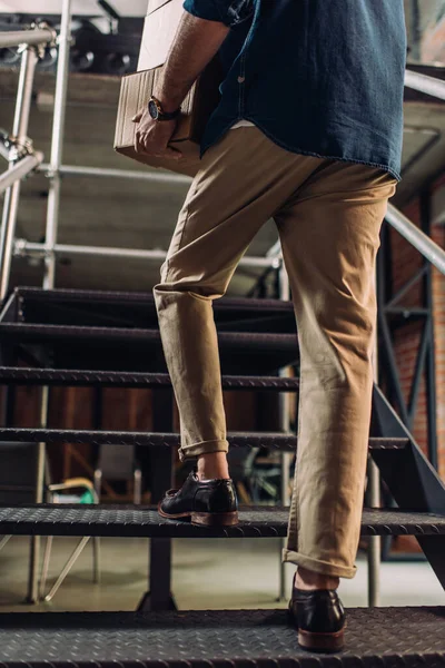 Ausgeschnittene Ansicht von Geschäftsmann, der Kisten hält, während er im Büro auf Treppen geht — Stockfoto