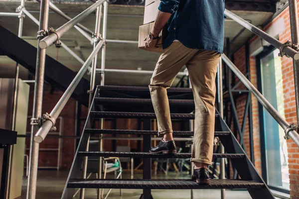 Cropped view of businessman holding carton boxes while walking on stairs in office — Stock Photo