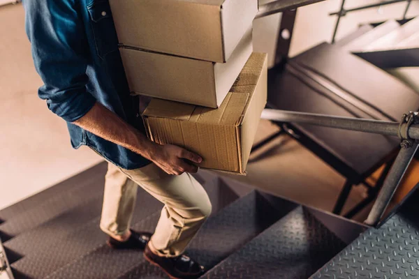 Partial view of businessman holding carton boxes and walking on stairs in office — Stock Photo