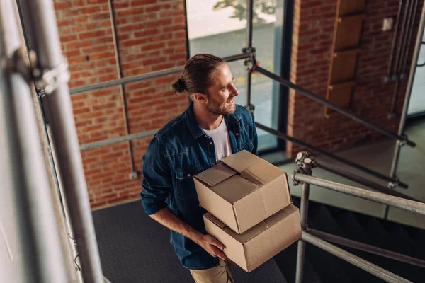 Foyer sélectif d'homme d'affaires souriant tenant des boîtes et marchant sur les escaliers dans le nouveau bureau — Photo de stock