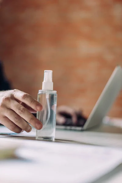 Abgeschnittene Ansicht von Geschäftsmann, der Flasche mit Händedesinfektionsmittel berührt und Laptop benutzt — Stockfoto