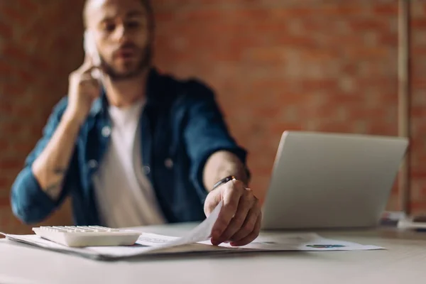 Вибірковий фокус бізнесмена розмовляючи на смартфоні і беручи документ біля ноутбука в офісі — стокове фото