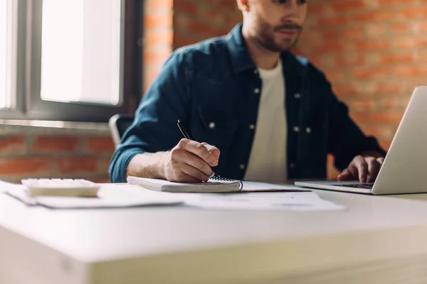 Вибірковий фокус бізнесмена, що пише в блокноті біля ноутбука в офісі — стокове фото