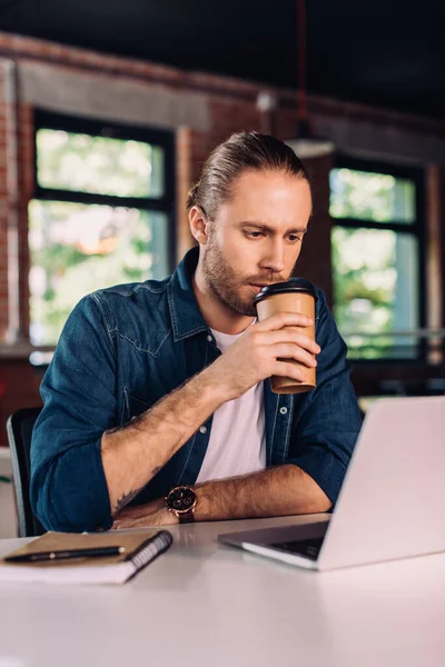 Focalizzazione selettiva dell'uomo d'affari che beve caffè per andare a guardare il computer portatile in ufficio — Foto stock