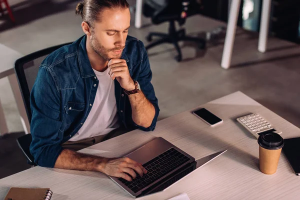 Pensive businessman using laptop near smartphone with blank screen and paper cup — Stock Photo