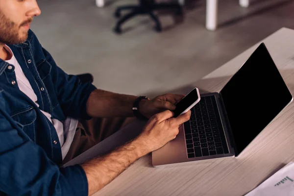 Обрезанный вид бизнесмена с помощью смартфона рядом с ноутбуком на столе — стоковое фото