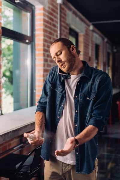 Handsome businessman talking on smartphone and spraying sanitizer on hand — Stock Photo