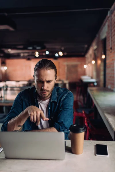 Selective focus of businessman pointing with finger at laptop near smartphone and paper cup — Stock Photo