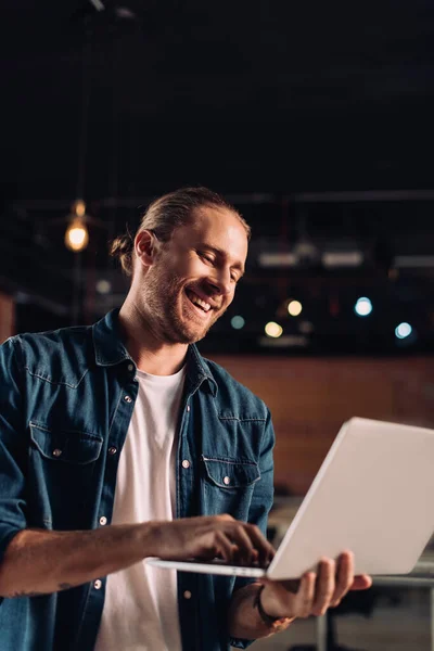 Empresário alegre segurando e usando laptop no escritório moderno — Fotografia de Stock