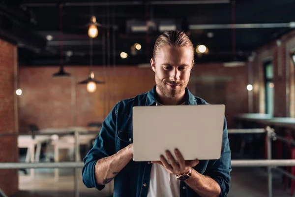 Бородатый бизнесмен держит и использует ноутбук в современном офисе — стоковое фото