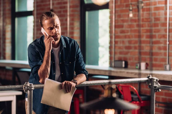 Вибірковий фокус бородатого бізнесмена, який розмовляє на смартфоні і тримає теку в офісі — стокове фото
