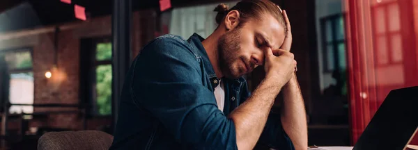 Cosecha panorámica de hombre de negocios cansado sentado cerca de la computadora portátil con pantalla en blanco en la oficina - foto de stock