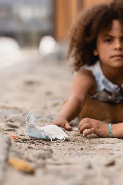 Selektiver Fokus armer afrikanisch-amerikanischer Kinder, die schmutzige medizinische Maske in der Nähe ihrer lockigen Schwester erreichen — Stockfoto