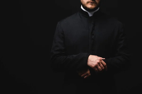 Обрезанный вид священника, стоящего изолированно на черном — стоковое фото