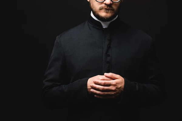 Обрезанный вид священника с сжатыми руками, изолированными на черном — стоковое фото