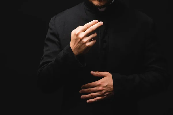 Abgeschnittene Ansicht eines Priesters, der gestikuliert, während er isoliert auf schwarz betet — Stockfoto