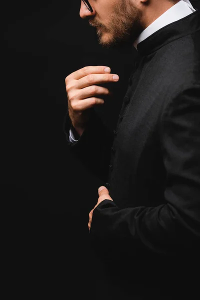 Side view of priest gesturing and praying isolated on black — Stock Photo