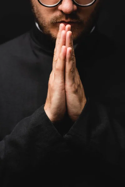 Partial view of bearded priest with praying hands isolated on black — Stock Photo