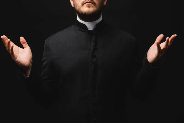 Vue recadrée du prêtre avec les mains tendues isolées sur noir — Photo de stock