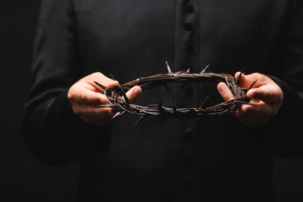 Cropped view of priest holding wreath with spikes isolated on black — Stock Photo
