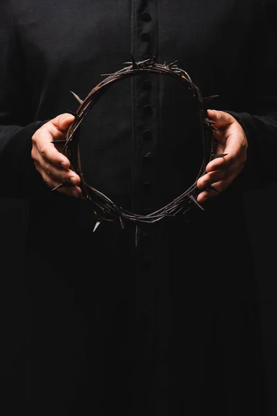 Cropped view of pastor holding wreath with spikes isolated on black — Stock Photo