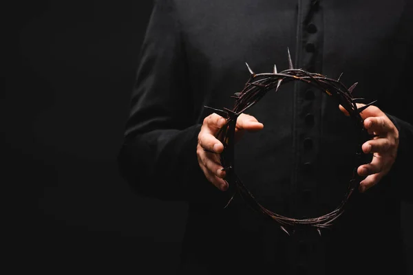 Cropped view of pastor holding wreath with spikes in hands isolated on black — Stock Photo