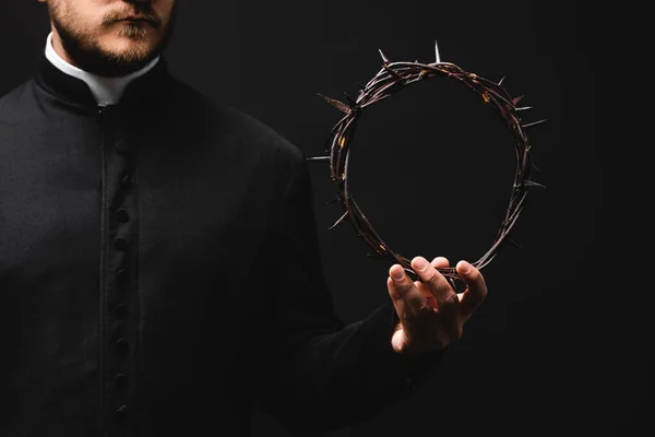 Cropped view of pastor holding wreath with spikes in hand isolated on black — Stock Photo