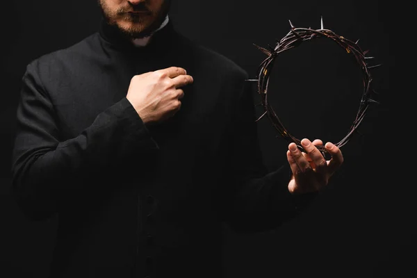 Cropped view of priest holding wreath with spikes in hand while praying isolated on black — Stock Photo
