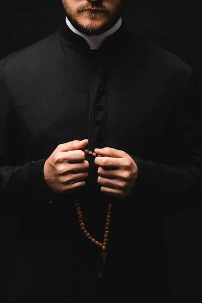 Vista recortada del sacerdote sosteniendo cuentas de rosario aisladas en negro - foto de stock