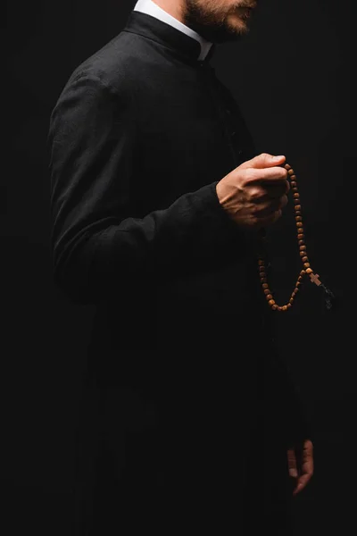 Abgeschnittene Ansicht des Priesters, der Rosenkranzperlen hält und isoliert auf schwarz steht — Stockfoto