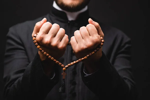 Foyer sélectif du pasteur tenant chapelet perles dans les mains et priant isolé sur noir — Photo de stock