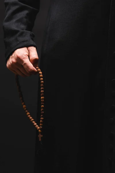 Partial view of pastor holding rosary beads in hand isolated on black — Stock Photo