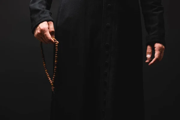 Vista parziale del sacerdote che tiene rosario perline in mano isolato su nero — Foto stock