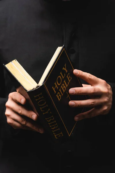 Visão parcial do pastor leitura bíblia sagrada isolado no preto — Fotografia de Stock