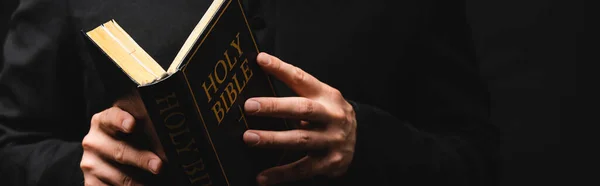 Horizontal image of pastor reading holy bible isolated on black — Stock Photo