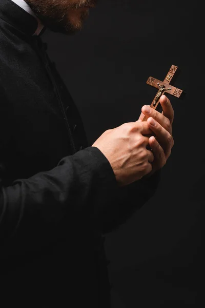 Vista recortada del sacerdote sosteniendo cruz de madera aislada en negro - foto de stock